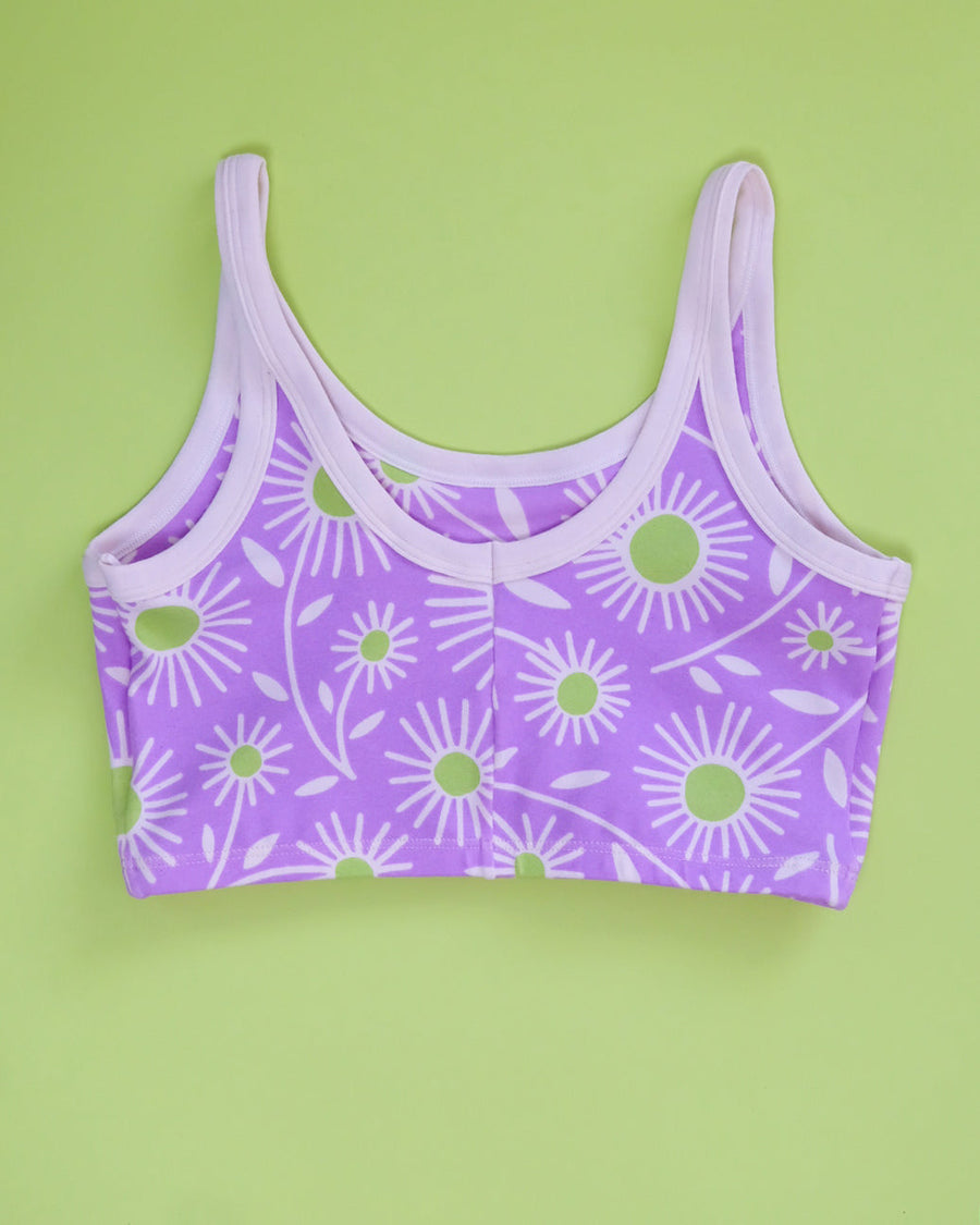 Flat lay product shot showing the front view of the purple Delia's Daisy organic cotton longline bra on a green backdrop.