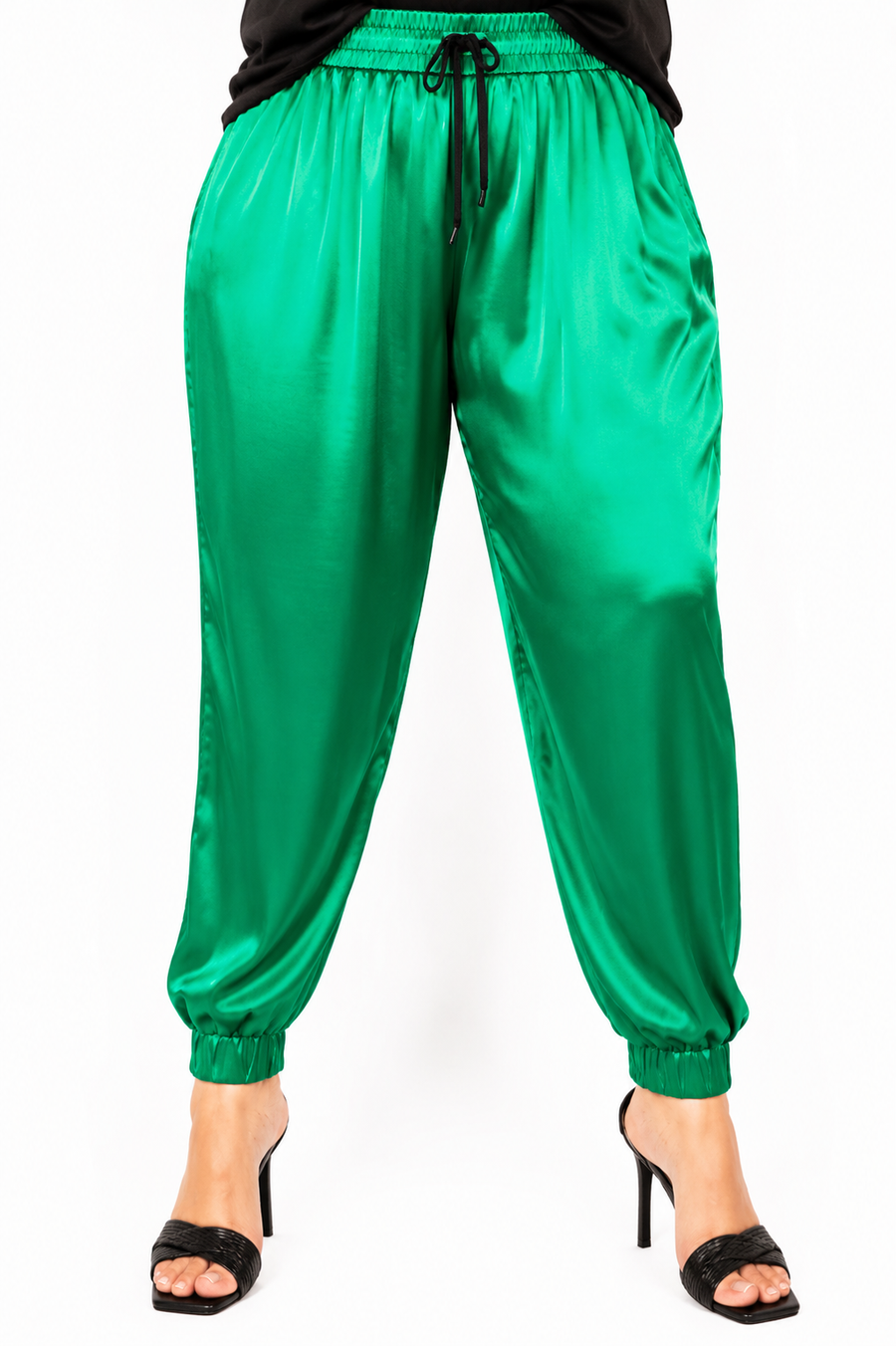 Front view close-up of a model wearing high-waisted emerald green Italian silk jogger pants with a black drawstring waist and elastic cuffed ankles.