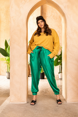 Full-length editorial portrait of a model standing in an archway wearing emerald green Italian silk jogger pants styled with a yellow sweater.