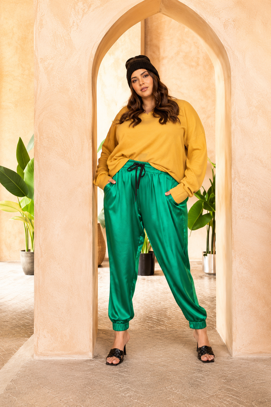Full-length editorial portrait of a model standing in an archway wearing emerald green Italian silk jogger pants styled with a yellow sweater.