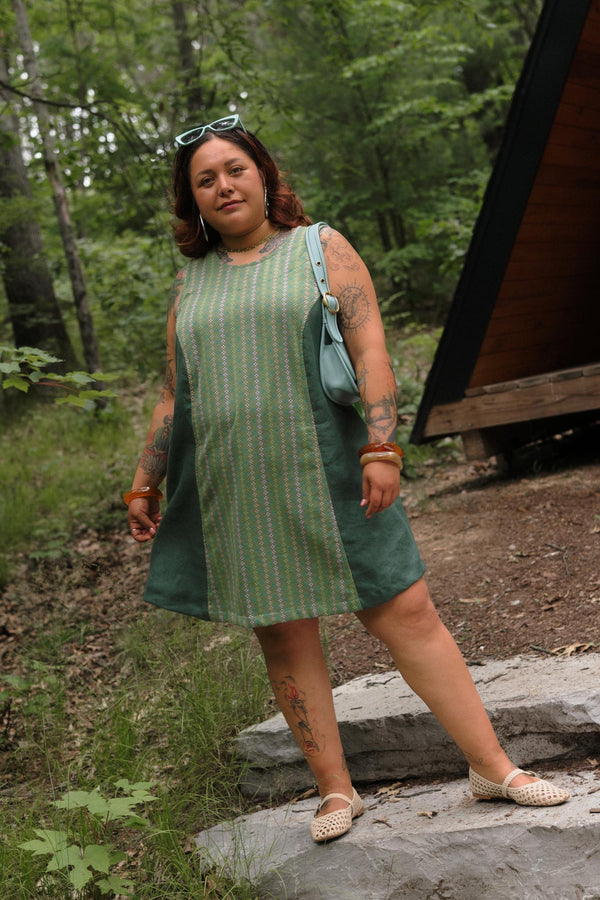 Full-length outdoor portrait of a model standing on stone steps wearing the sleeveless aloe green Beth A-line dress by Conscious Clothing.