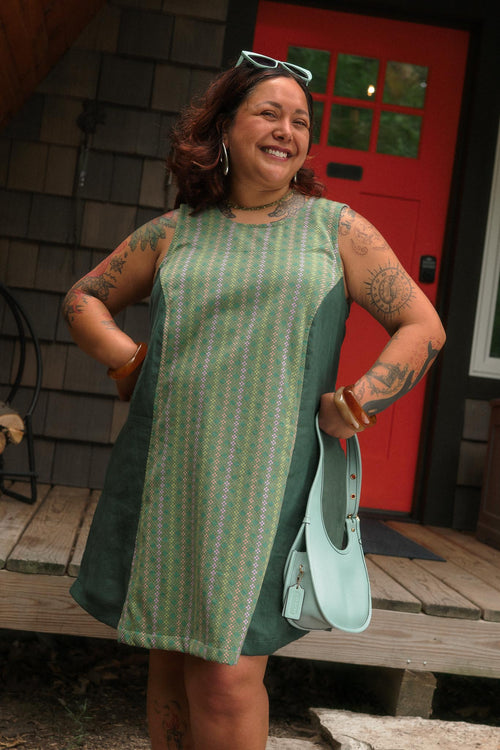 Front view of a model posing on a cabin porch in the relaxed-fit aloe green cotton and linen Beth Dress with princess seam details.