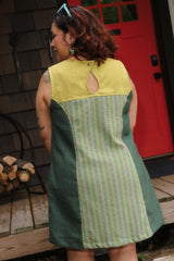 Rear view highlighting the keyhole snap closure and yellow contrast yoke on the sleeveless aloe green linen and cotton dress.