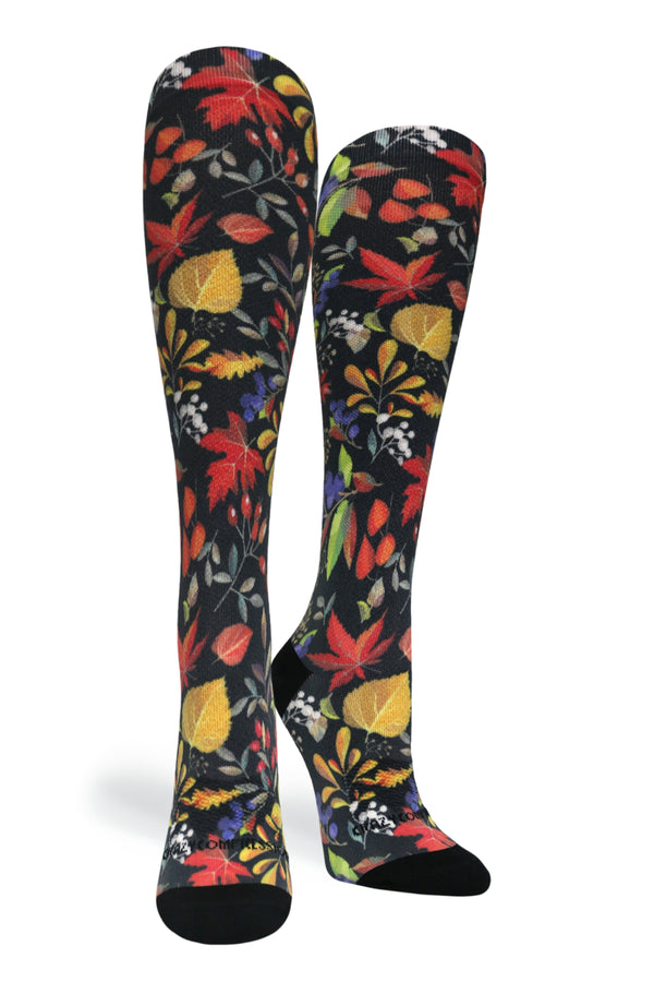 Studio shot of a pair of Crazy Compression Falls Back knee-high socks featuring an autumn leaf and botanical pattern on black fabric.