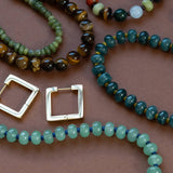 Overhead lifestyle arrangement showing the Green Margot Beaded Necklace alongside gold square hoop earrings and complementary gemstone jewelry.
