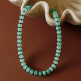 Flat lay product shot of the Green Margot Beaded Gemstone Necklace laid across a decorative beige shell dish.