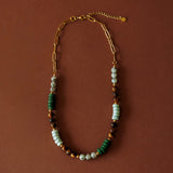 Flat lay product display of the Green Phoebe Necklace showing the mixed gemstones and gold PVD paperclip chain on a warm brown