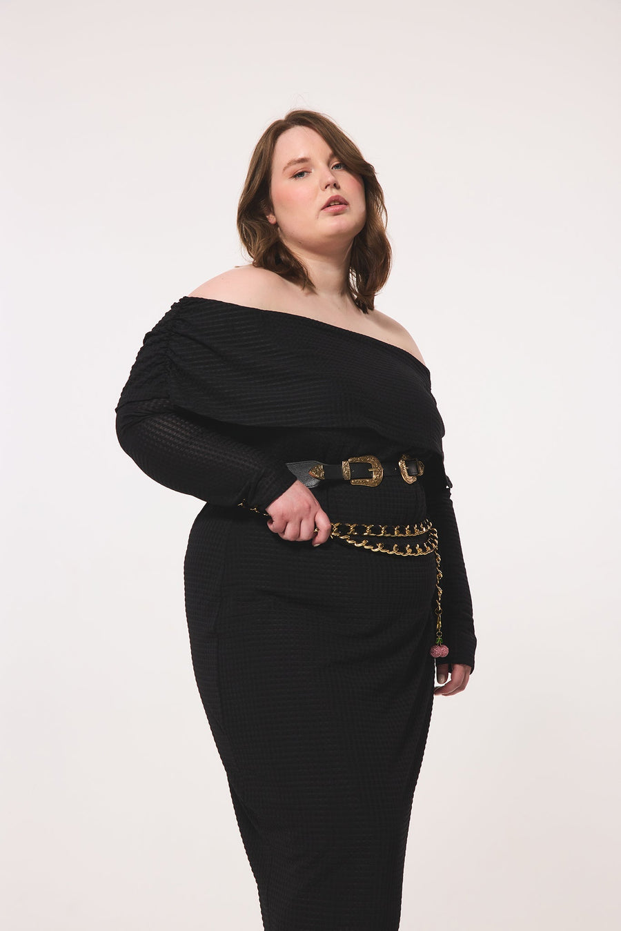 Three-quarter close-up view of a plus-size model highlighting the fold-over elastic neckline, unlined long sleeves, and double-belt styling of the geometric black dress.