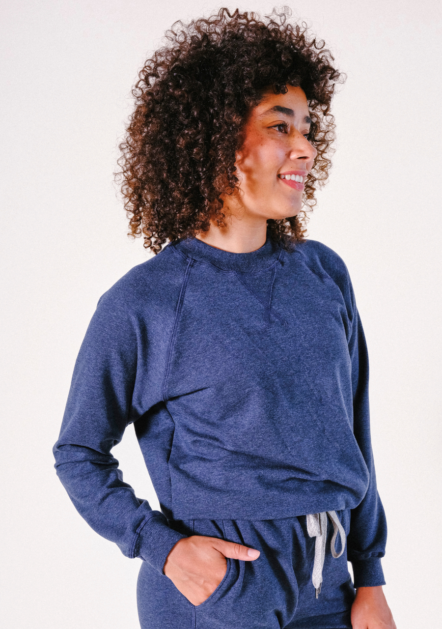 Three-quarter view of a smiling model posing in the blue heather organic cotton and Tencel Agnes Raglan Sweatshirt.