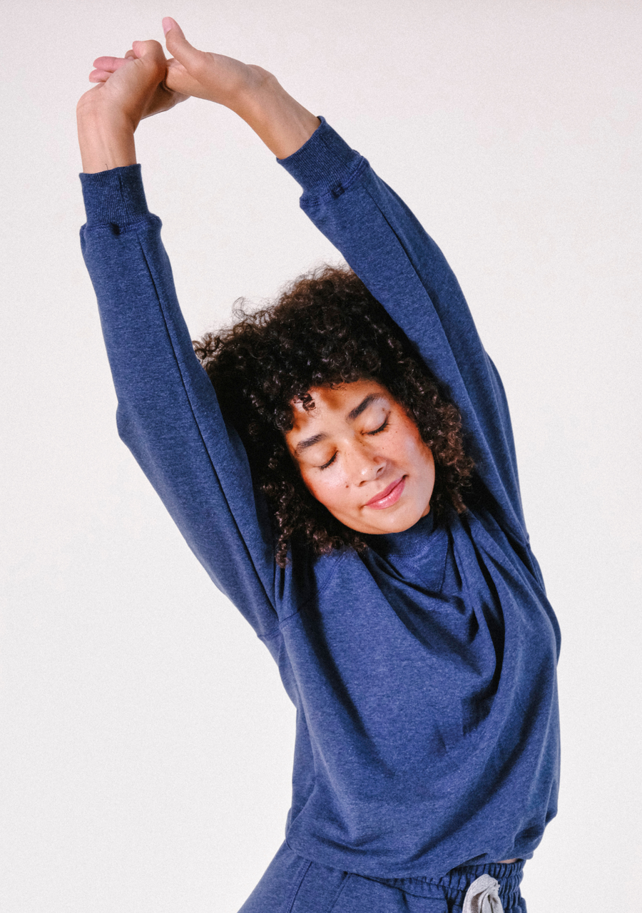 Model stretching her arms overhead while wearing the soft Poplinen Agnes Raglan Sweatshirt in Heather Lake.