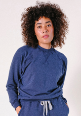 Front view portrait of a model with curly hair wearing the Poplinen Agnes Raglan Sweatshirt in Heather Lake blue.