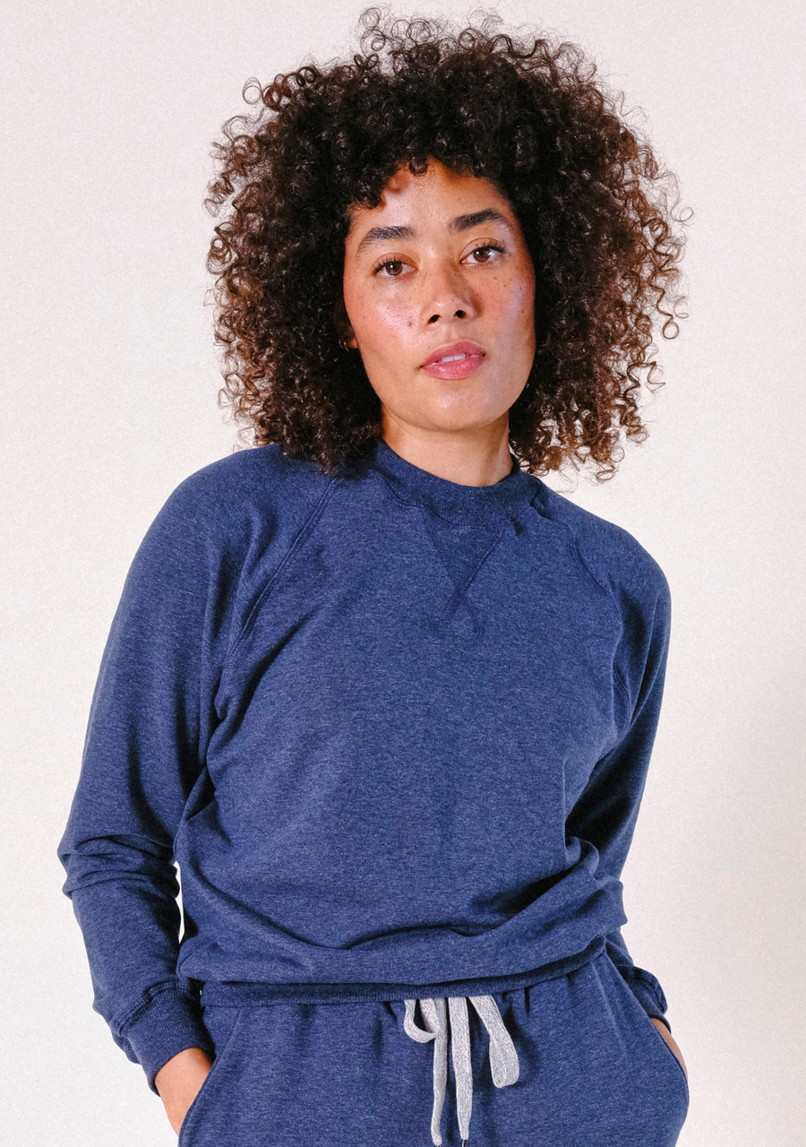Front view portrait of a model with curly hair wearing the Poplinen Agnes Raglan Sweatshirt in Heather Lake blue.
