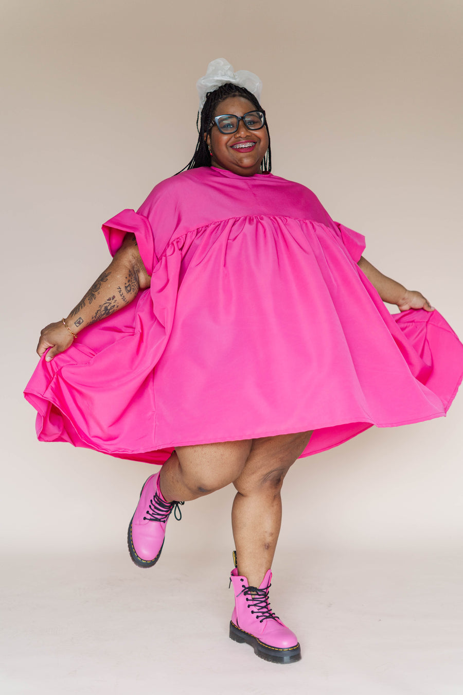 Full-length shot of a Black plus-size model wearing the hot pink voluminous Nettle Studios Mini Mushroom Dress with matching pink boots.