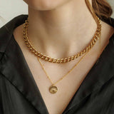 Model wearing the Sela Designs Parker gold link chain layered with a delicate gold sun pendant necklace against a black blouse.