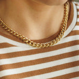 Close-up shot of a model wearing the Parker gold link chain necklace over a brown and white striped top.