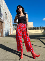 Full-body outdoor shot of model Mia wearing the red wide-leg Sondler Cat Skater Pant with a black tank top and red leather boots.