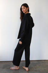 Side profile view of a dark-haired model showcasing the drape and length of the black wide-leg linen pants.