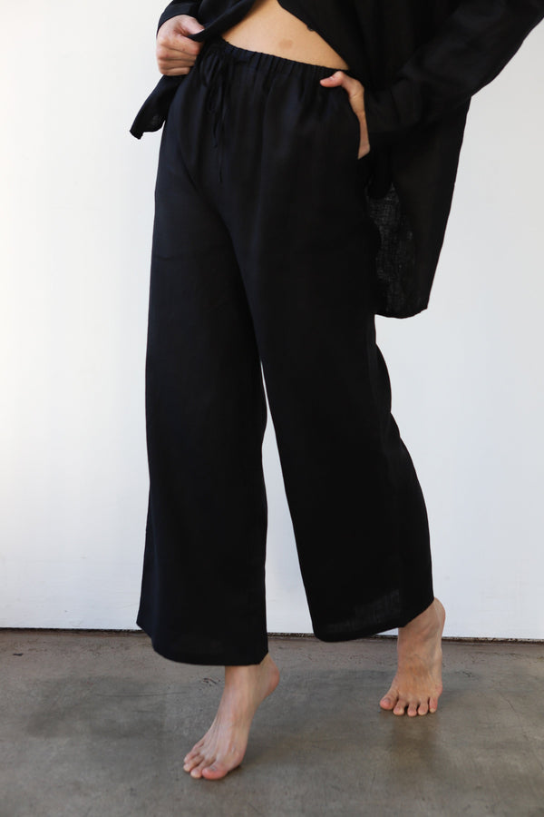 Mid-section detail photo showing the elastic waistband, front drawstring, and side pocket of the black linen pants.