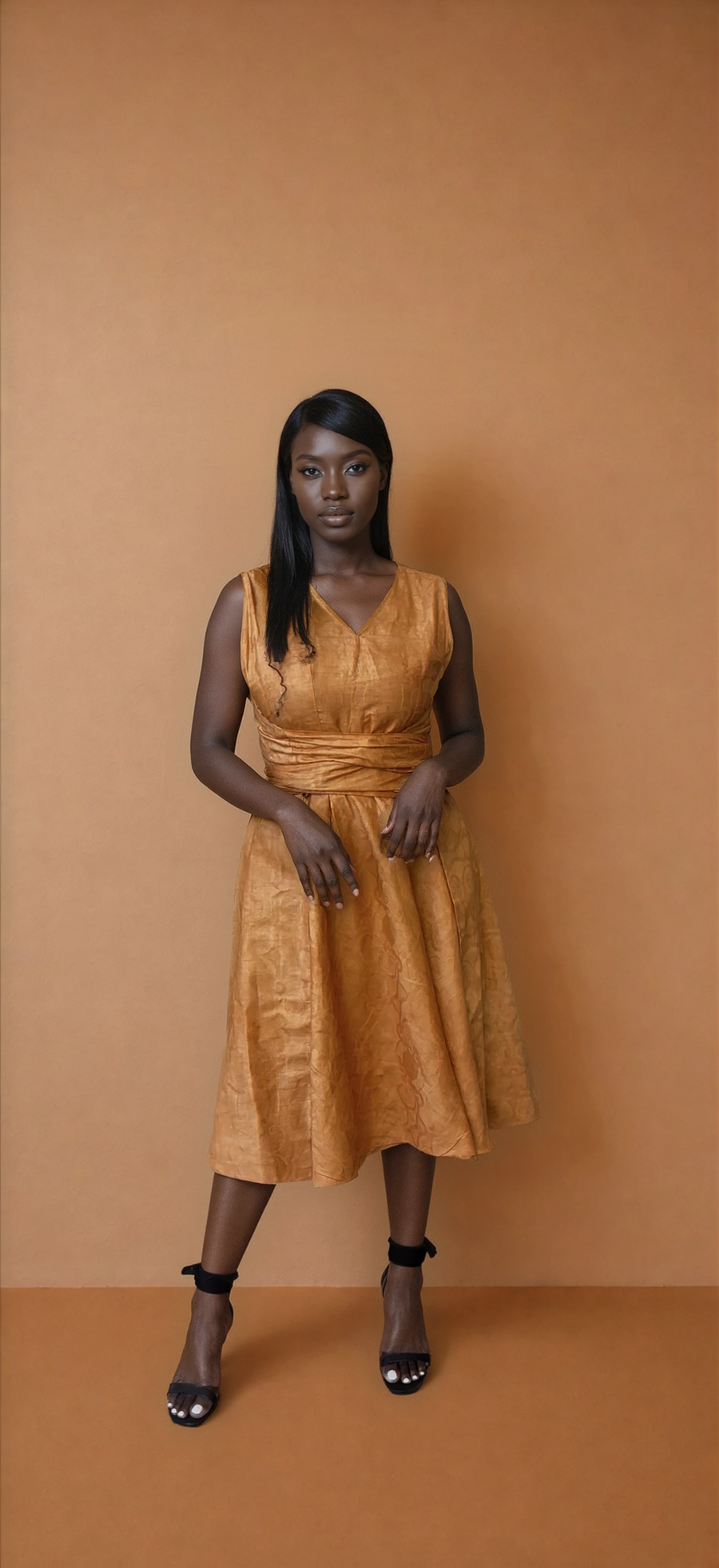 Full-length view of a model showcasing the reverse side of the Besida Palm Orange Reversible Dress in a solid, rich textured orange hue. The sleeveless, V-neck cotton midi dress is styled with a matching fabric waist wrap and black ankle-strap heels against a warm neutral studio backdrop.