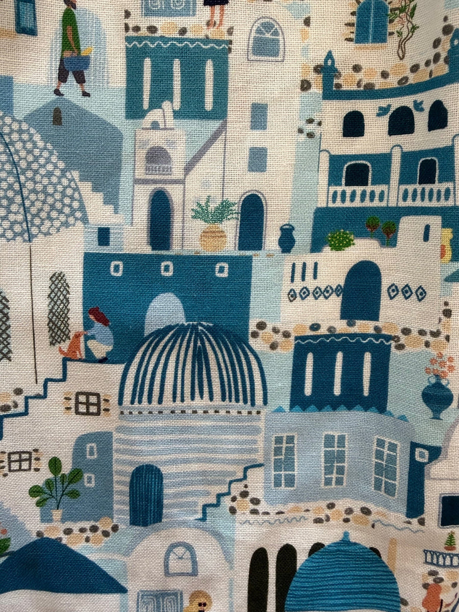 Close-up fabric pattern detail of the Retrolicious Santorini print showing blue and white Mediterranean buildings, domes, and arches on cotton fabric.