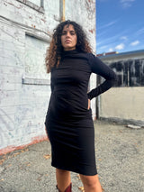 Three-quarter front view of model Sarah posing in the fitted black NOOWORKS Demi Dress styled with maroon cowboy boots.