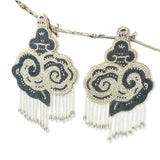 Pair of cloud-shaped hand-embroidered grey and white beaded statement earrings hanging from a tree branch.