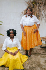 Models wearing the Besida Orange Palm Reversible Wrap Skirt styled with white button-up shirts, featuring orange and yellow colorways.
