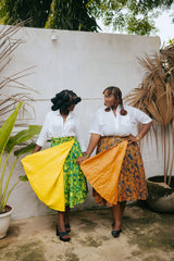 Models wearing the Besida Orange Palm Reversible Wrap Skirt styled with white button-up shirts, featuring orange and yellow colorways.