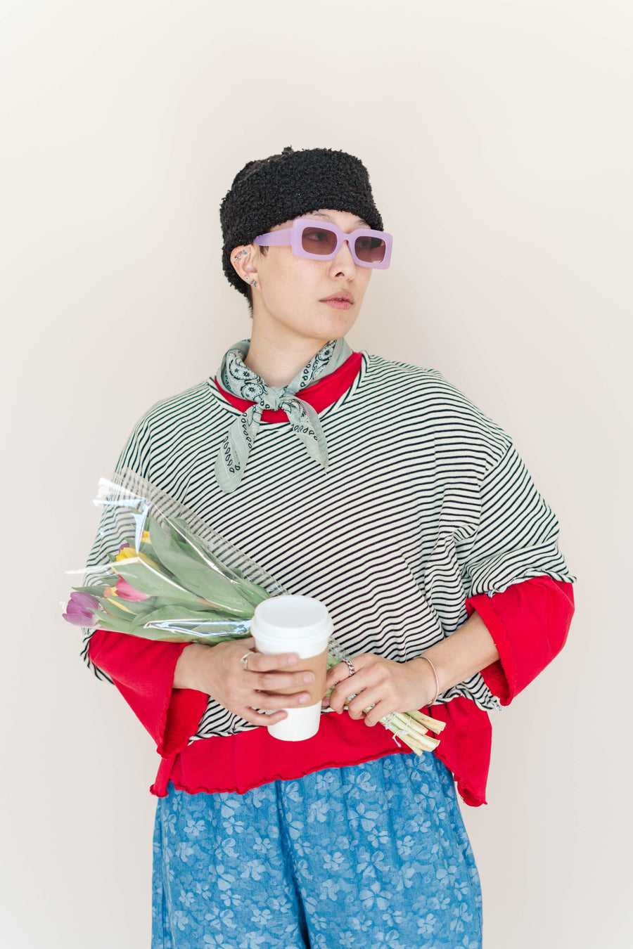 Model wearing Nettle Studios Lemon Water Striped Favorite Tee layered over a red long-sleeve top, holding coffee and flowers.