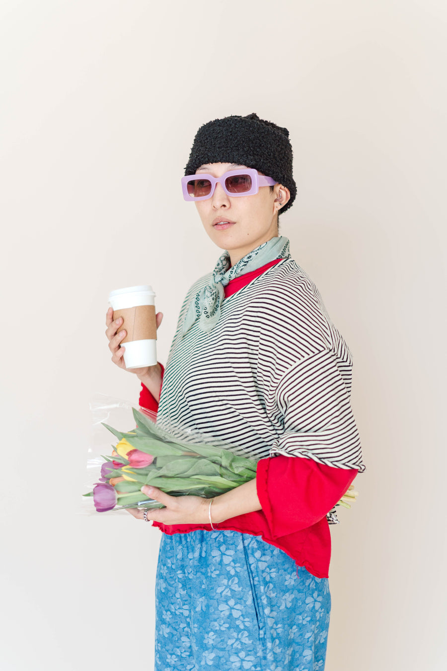 Side profile of model in Nettle Studios striped cropped t-shirt layered over red sleeves with purple sunglasses.
