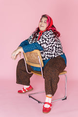Full-length studio shot of model Angelina seated on a chair wearing the Dizzy Favorite Tee layered over a long-sleeve top, paired with leopard print trousers.