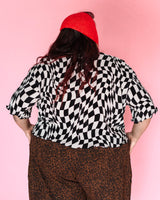 Back view of model Angelina wearing the black and white wiggly checker cropped tee and a red knit bonnet, showing the slouchy fit and merrow hem.