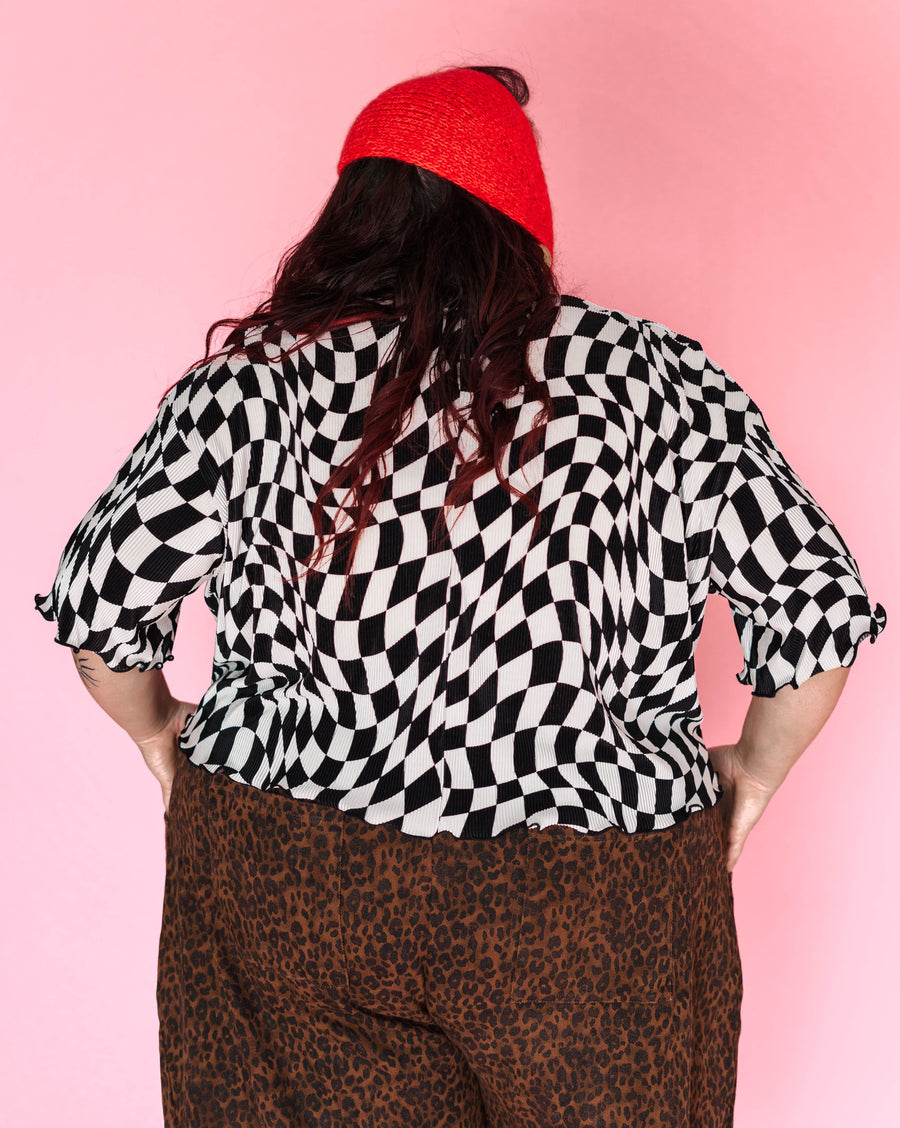Back view of model Angelina wearing the black and white wiggly checker cropped tee and a red knit bonnet, showing the slouchy fit and merrow hem.