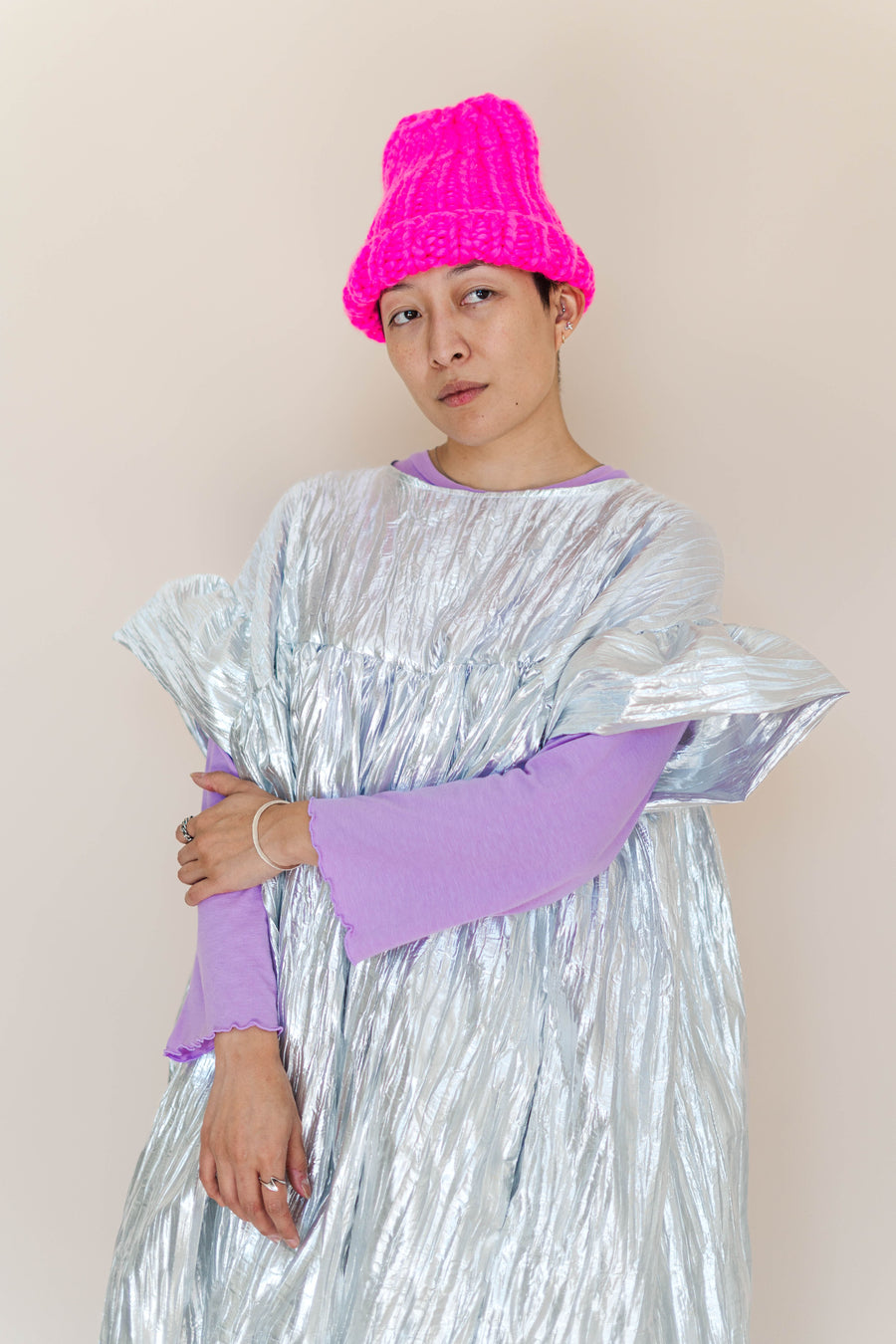 Medium studio portrait of model Madison layered in the Nettle Studios Silver Metallic Mushroom Dress over a lilac long-sleeve tee and accessorized with a hot pink beanie.