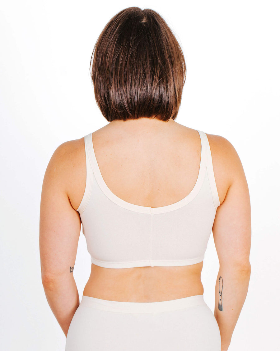 Rear view portrait showcasing the scoop back fit and flat bottom band of a cream organic cotton longline bra.