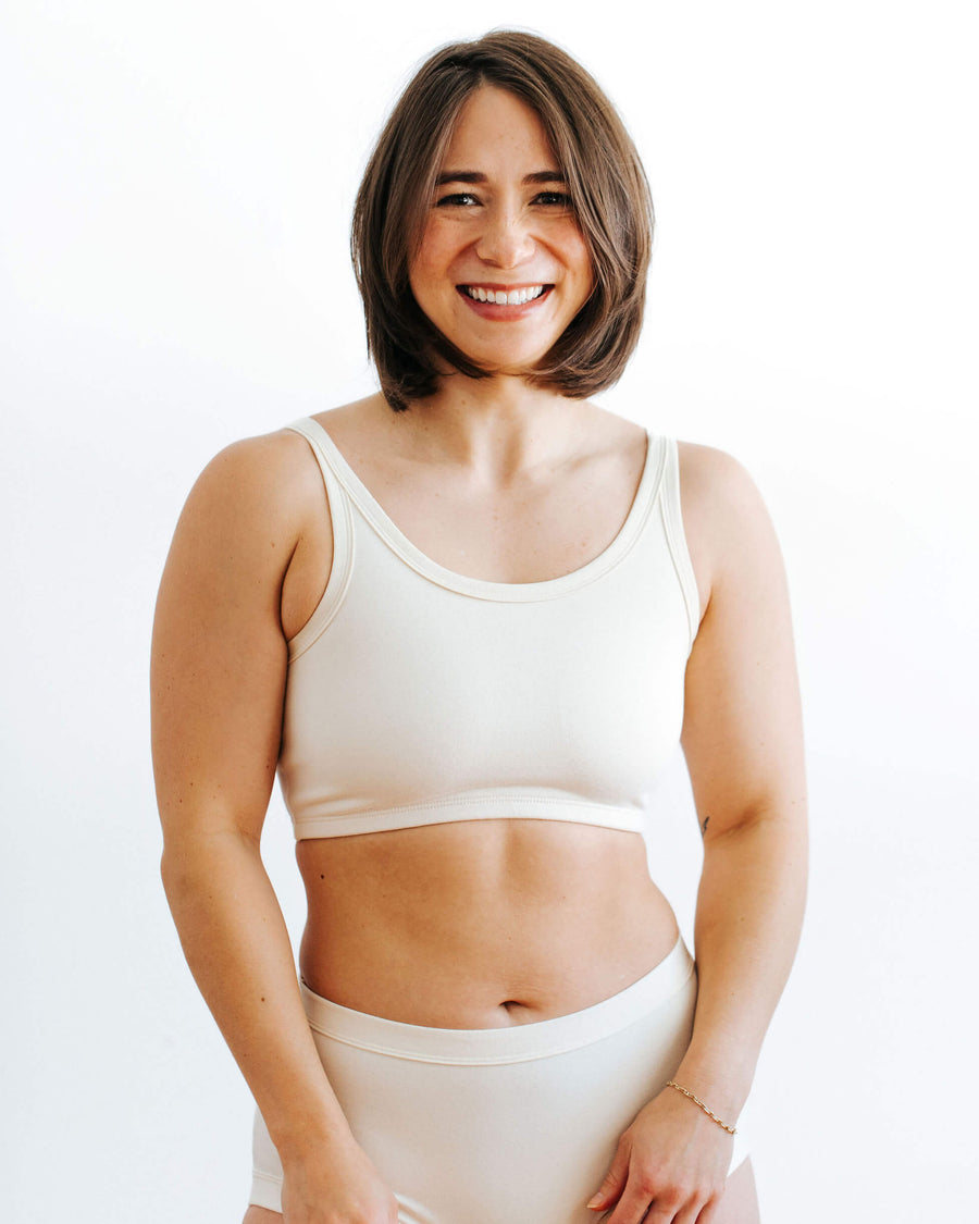 Front view studio portrait of a smiling brunette model wearing a cream-colored organic cotton longline bra.