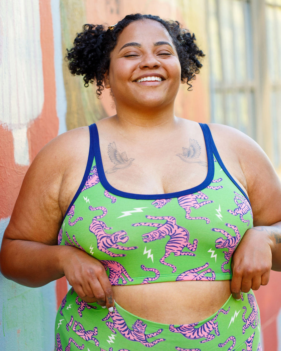 Front portrait of a smiling model wearing the Thunderpants US Longline Bra in Electric Tiger green with pink tigers and navy trim.