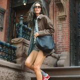  Model walking down brownstone steps carrying the STATE Bags Luna Crossbody styled with a casual jacket and shorts.