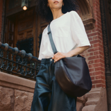 Low-angle street style portrait of a model wearing the black Luna Crossbody over a white tee and dark pants.