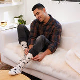 Man sitting on a sofa wearing Conscious Step Socks That Save Cats styled with jeans and a plaid flannel shirt.