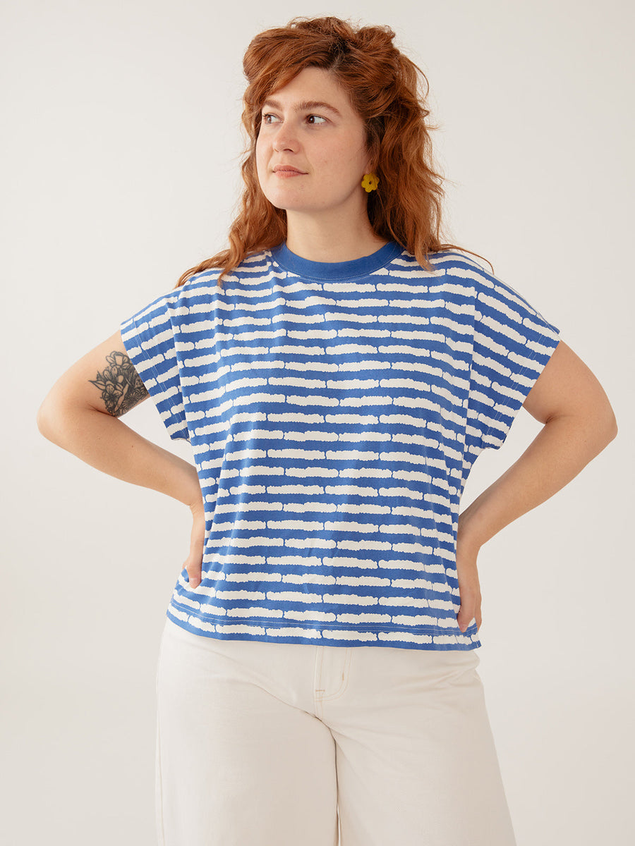 Model with red hair wearing the Mata Traders Caitlin Top in cobalt split stripe, paired with white wide-leg trousers.