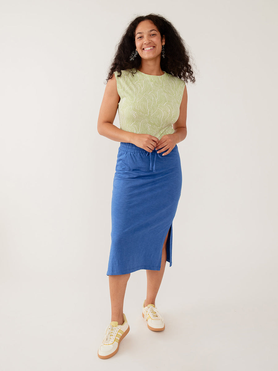 Model wearing the Mata Traders Isla Skirt in cerulean blue organic cotton slub knit, paired with a green printed top and sneakers.