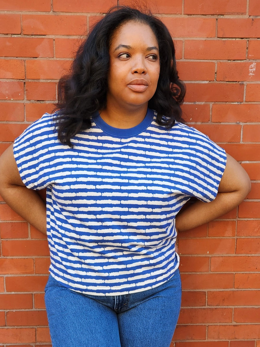 Model posing against a red brick wall in the boxy cobalt blue and white striped Caitlin drop-shoulder tee.