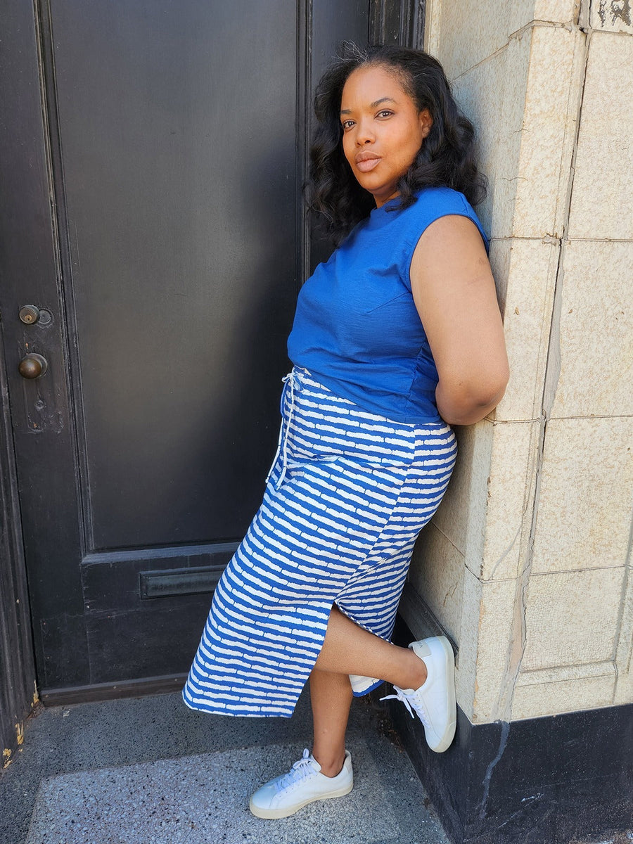 Model wearing the cobalt split stripe Isla midi skirt leaning against a doorway, paired with white sneakers.