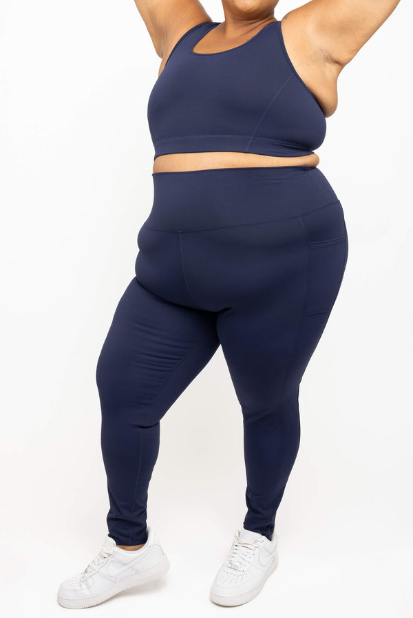 A plus-size Woman wearing Superfit Hero SuperHold high-waisted navy ankle leggings with side pockets and white sneakers  