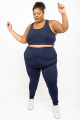 Full-body view of a model dancing in the navy SuperHold Racerback Sports Bra paired with matching high-waisted navy leggings and white sneakers.