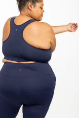 Back view of a plus-size model stretching her arm, highlighting the racerback fit and supportive band of the navy sports bra.