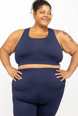 Front view of a model posing with hands on hips wearing the full-coverage navy SuperHold racerback sports bra and matching navy leggings.
