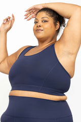 Close-up shot of a smiling plus-size model raising her arms while wearing the navy blue SuperHold Racerback Sports Bra.
