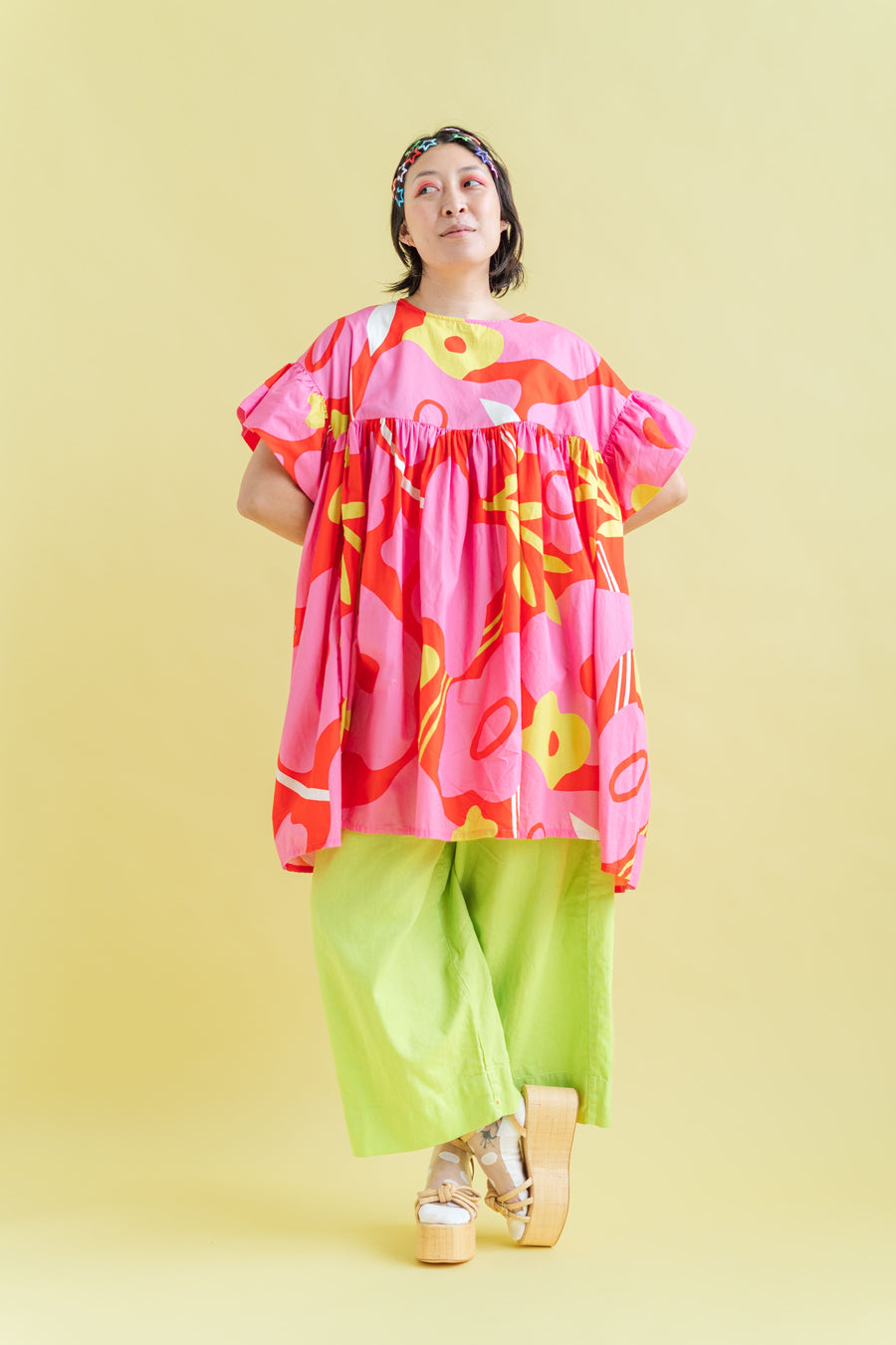 Studio portrait of a model crossing her legs wearing Limeade Linen Mid Easy Pants styled with a vibrant pink and orange floral tunic and platform sandals.